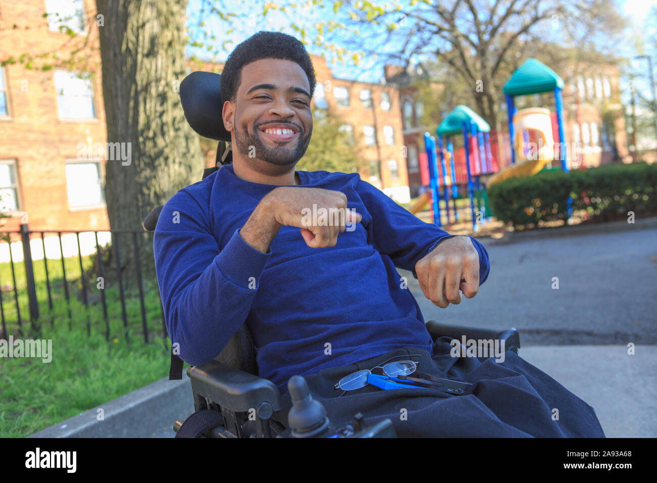 Felice uomo afroamericano con paralisi cerebrale usando il suo potere sedia a rotelle all'esterno Foto Stock