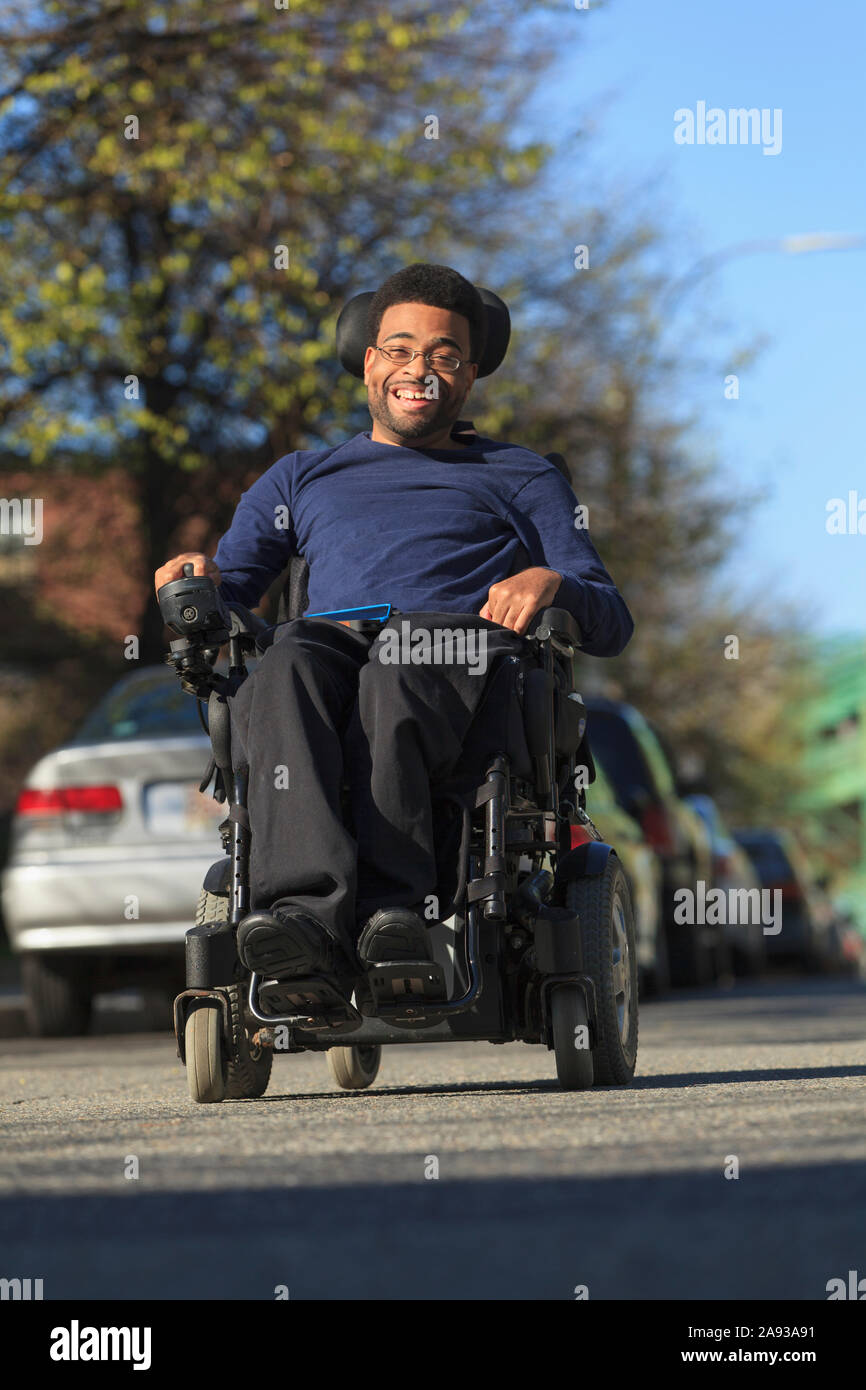 Felice uomo afroamericano con paralisi cerebrale usando il suo potere sedia a rotelle all'esterno Foto Stock