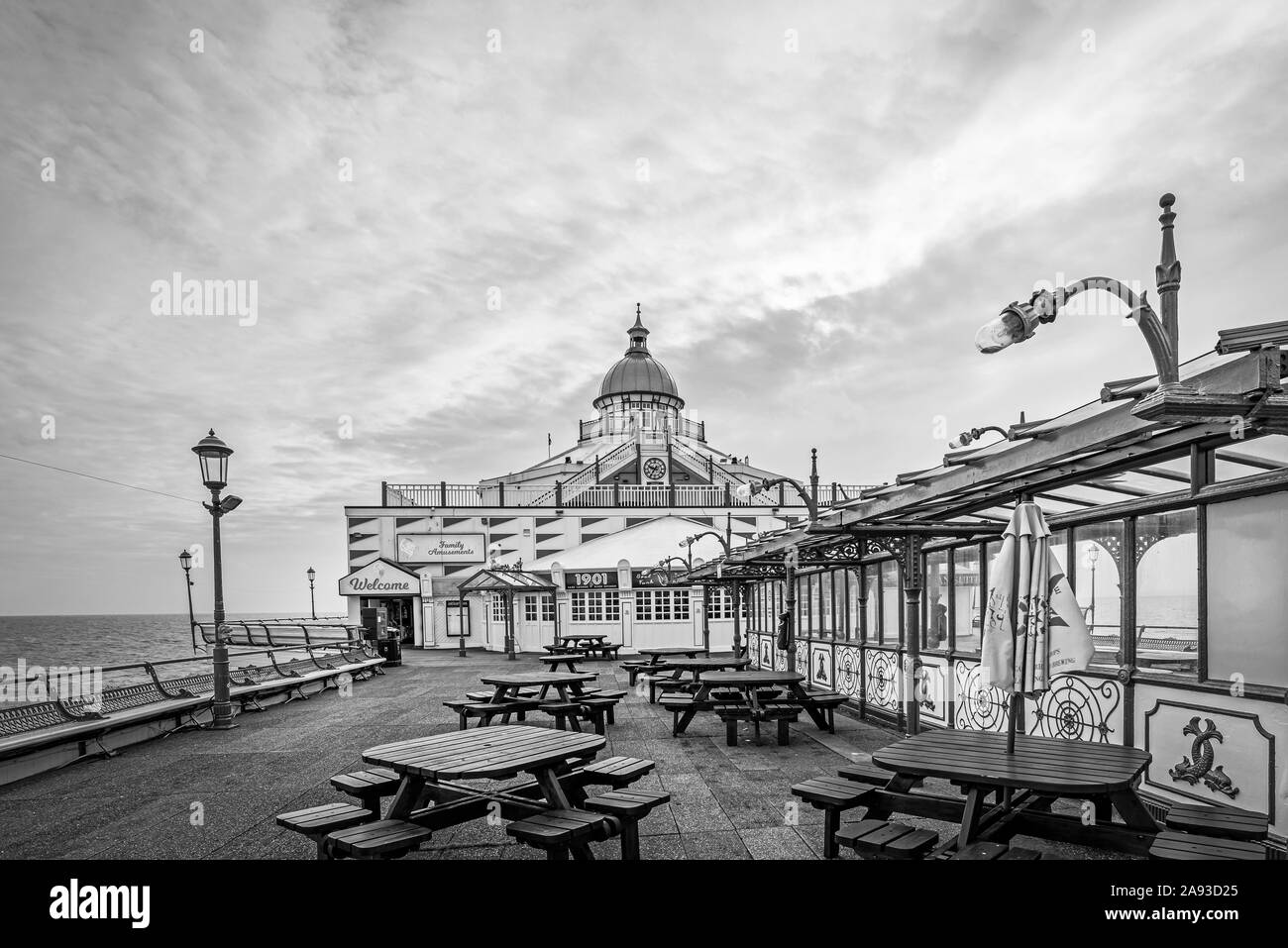 Eastbourne Pier con una fila di panche e suite. Il pavimento in legno conduce al fine edificio con una cupola giallo e un cielo nuvoloso è sopra la testa. Foto Stock