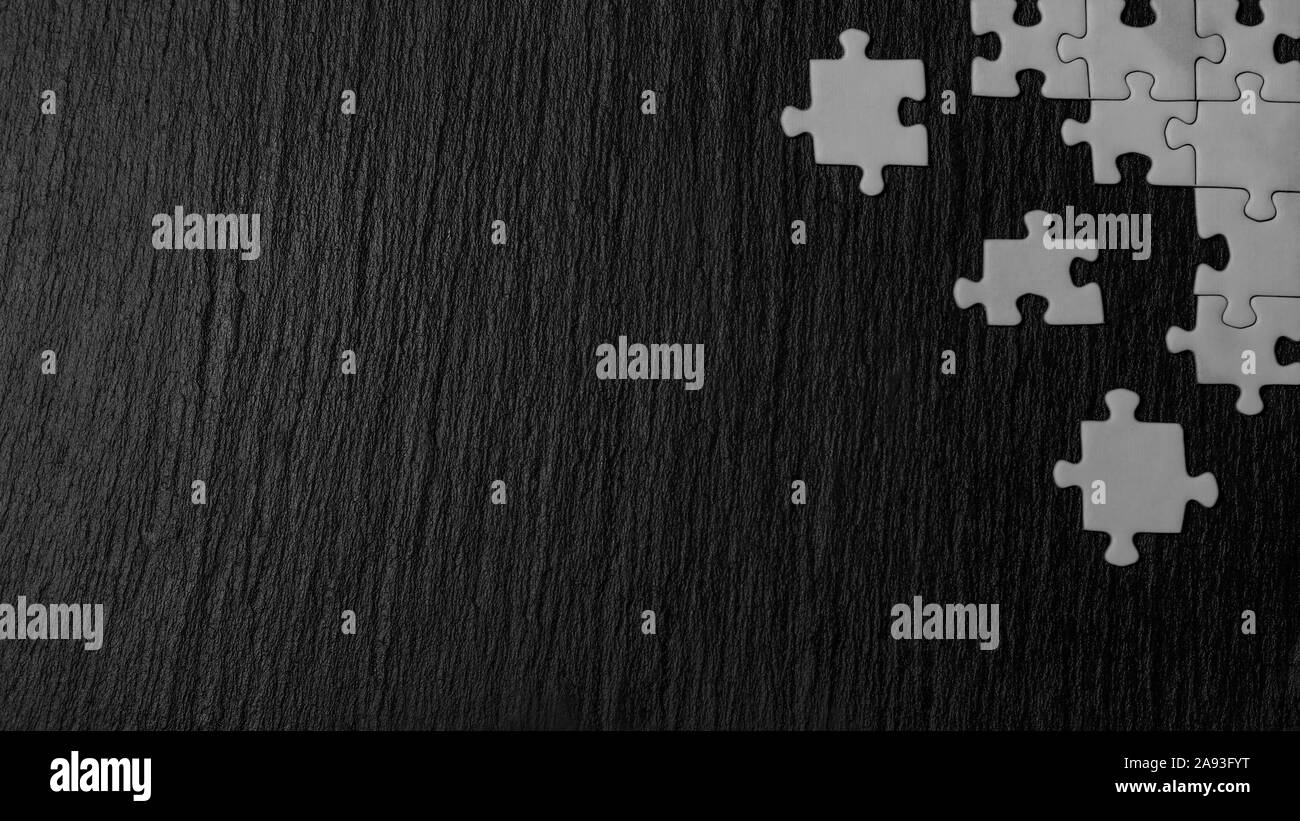 Puzzle bianco nell'angolo dell'immagine su un nero pietra naturale sfondo di ardesia. Un telaio con uno spazio vuoto per la tua descrizione. Foto Stock