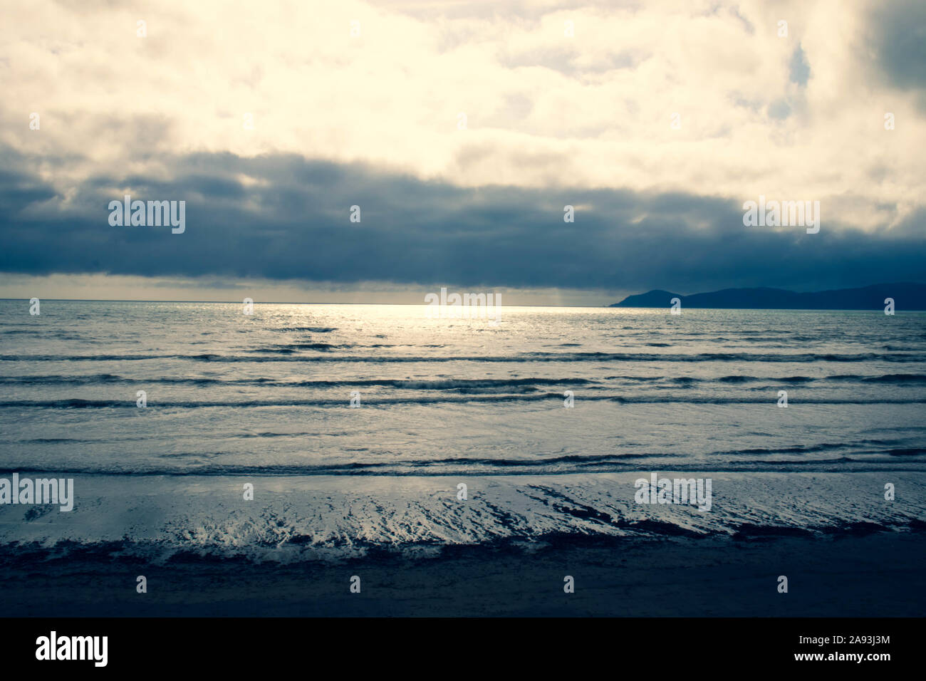 Drammatica cielo nuvoloso con lieve sunburst guardando fuori di Kapiti Island e oltre lo stretto di Cook da Raumati Beach, Wellington, Nuova Zelanda Foto Stock