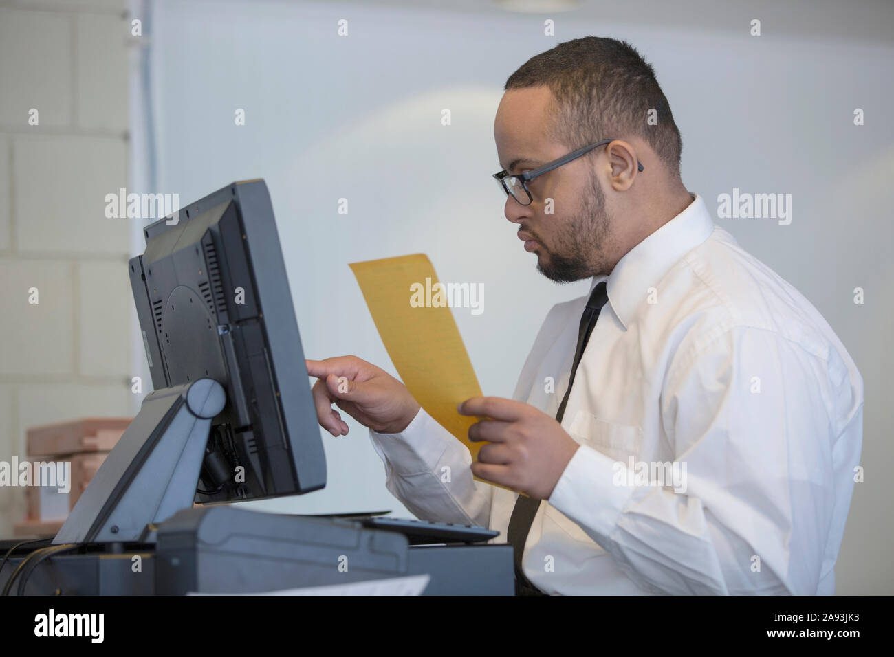 L'uomo afroamericano con la sindrome di Down come un cameriere che suona su una vendita sul calcolatore Foto Stock