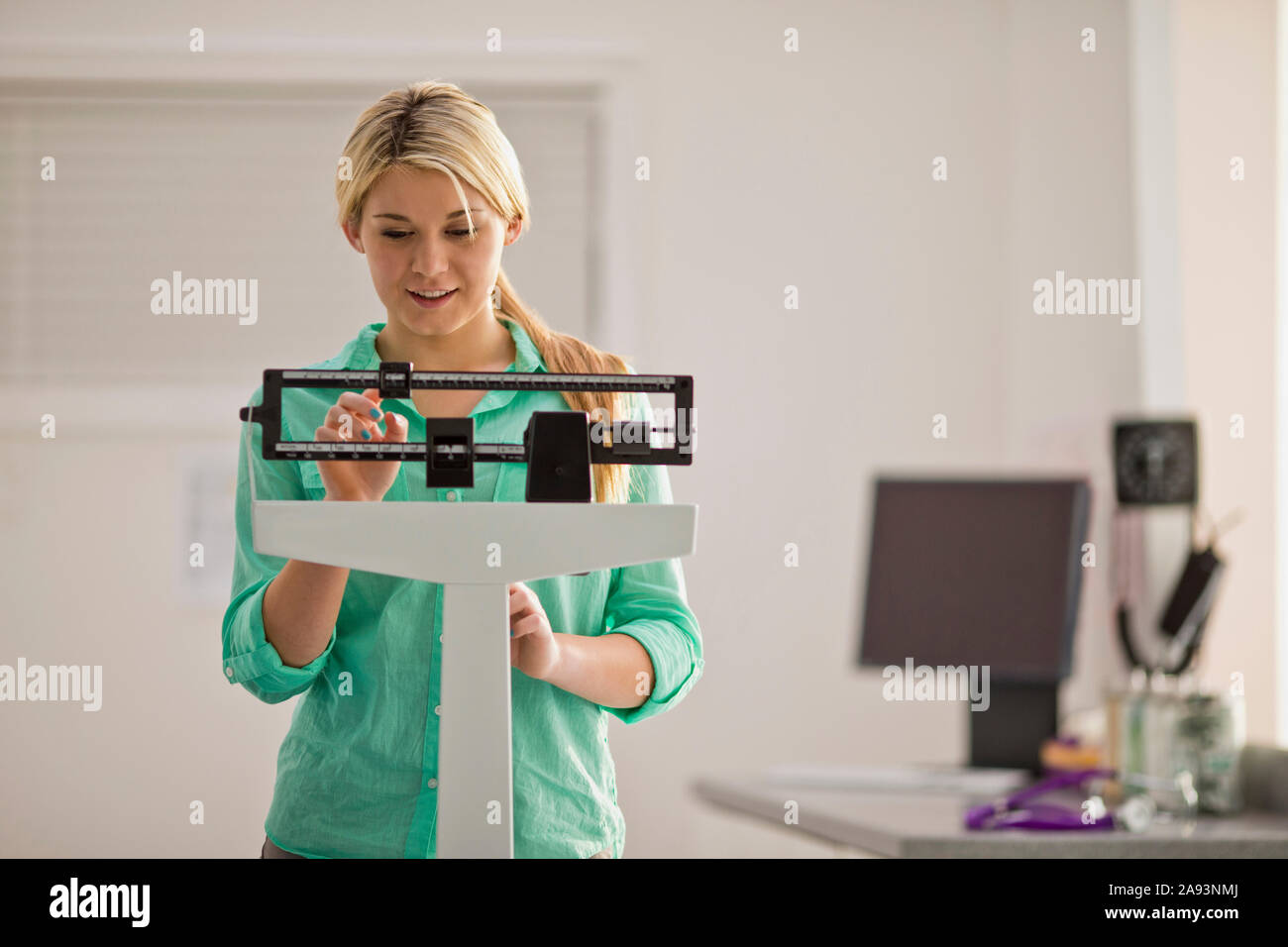 Sorridente giovane donna che si concentra mentre regola il vetrino sopra una bilancia medica mentre all'interno dell'ufficio del medico Foto Stock