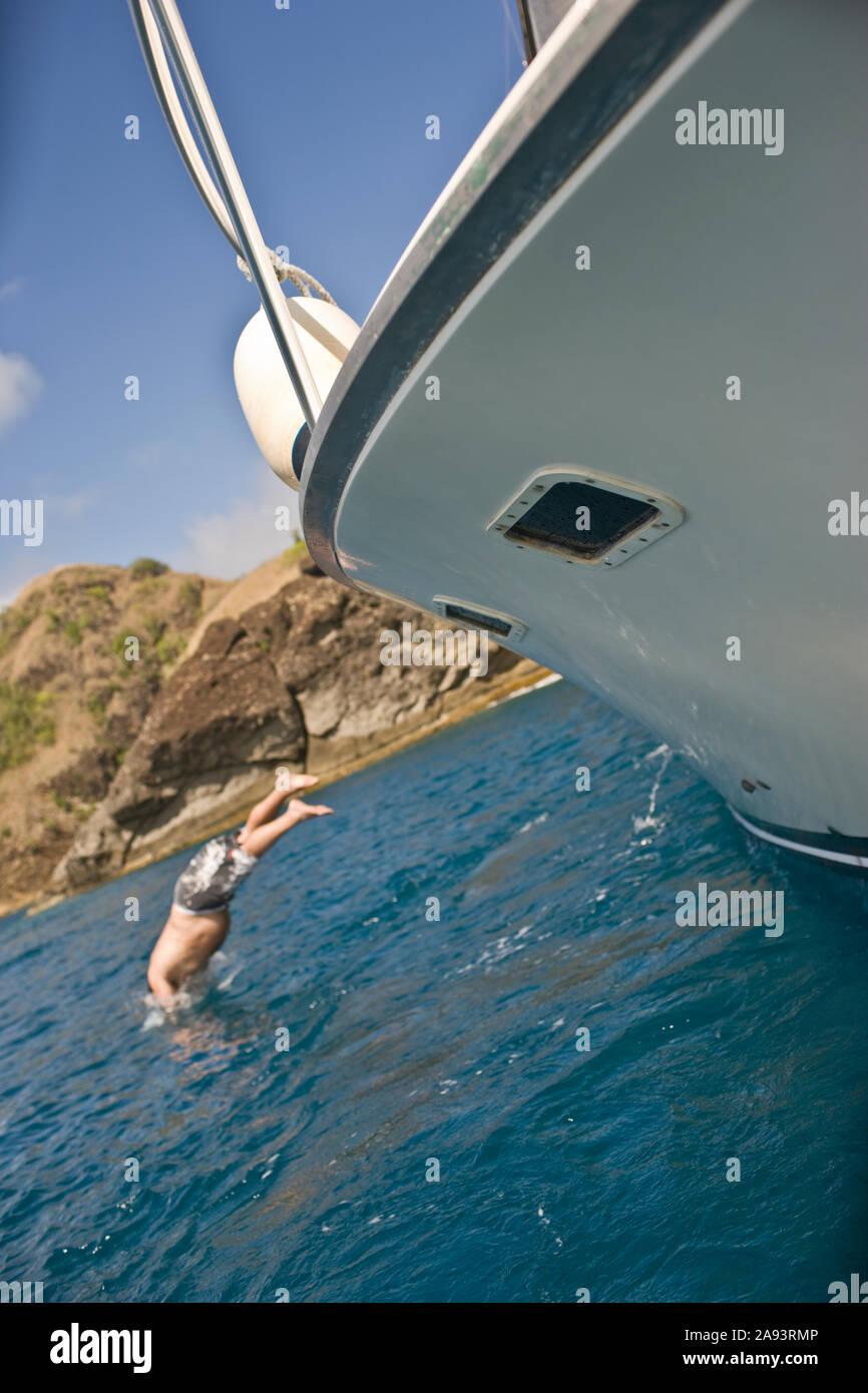 L'uomo le immersioni fuori dalla parte laterale di una barca ormeggiata vicino alla costa. Foto Stock
