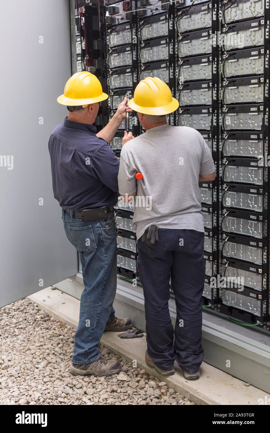 Gli ingegneri di energia di collegamento batterie di storage per il backup di potenza ad un impianto di potenza elettrico Foto Stock