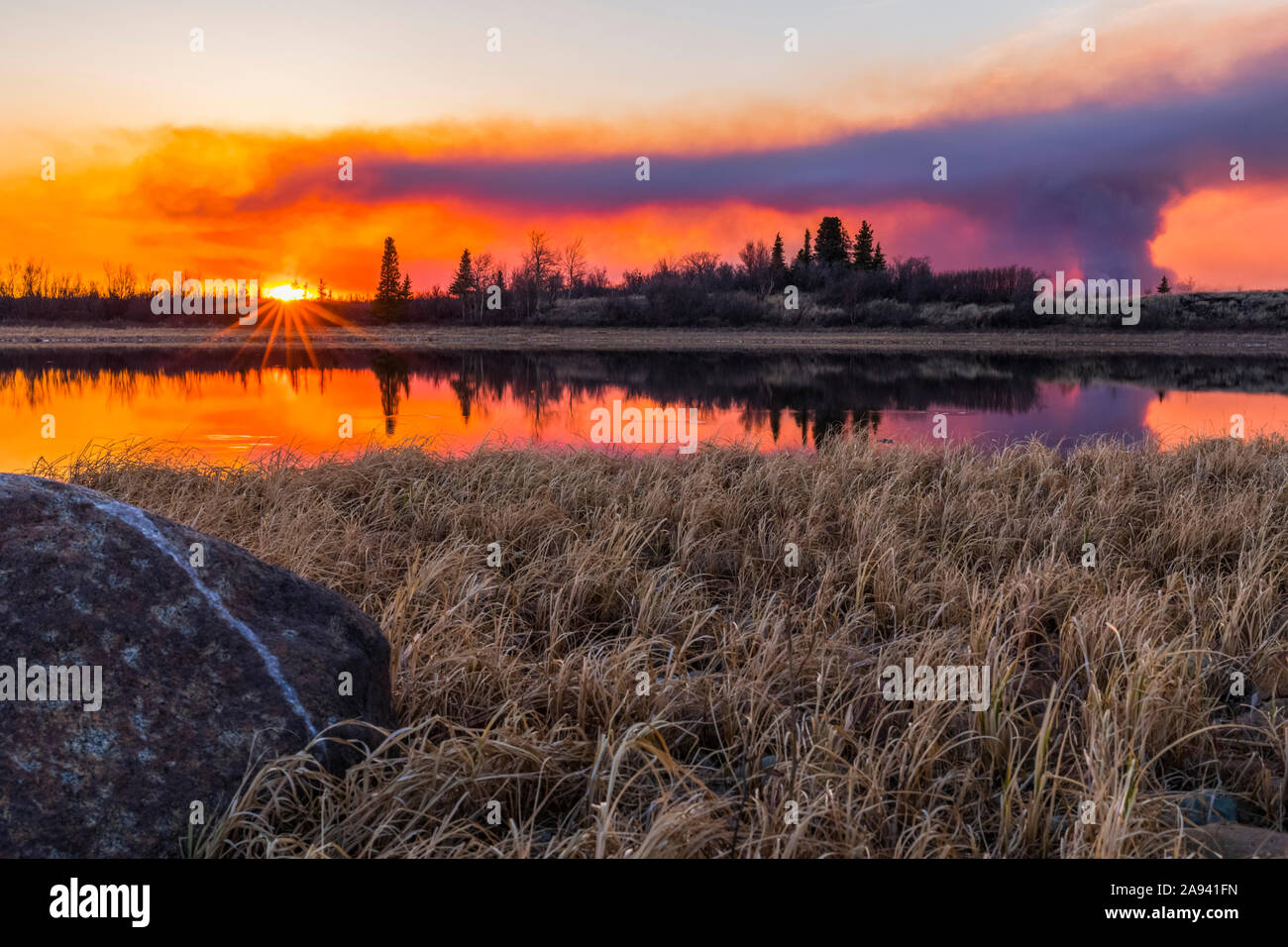 Un pennacchio di fumo che sorge dall'incendio dei 2019 laghi dell'Oregon si riflette in un lago al tramonto, a sud di Delta Junction; Alaska, Stati Uniti d'America Foto Stock