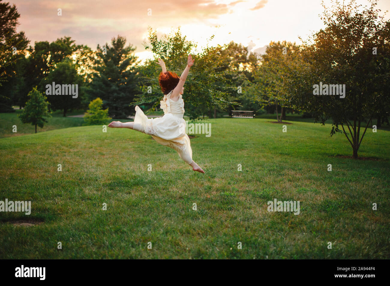 Una gioiosa giovane ballerino, illuminate dalla luce del sole, salti in un parco al tramonto Foto Stock