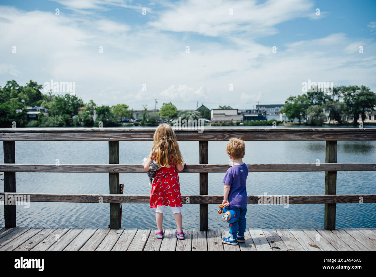 Due bambini stand ad un molo e guardare fuori in un stagno. Foto Stock