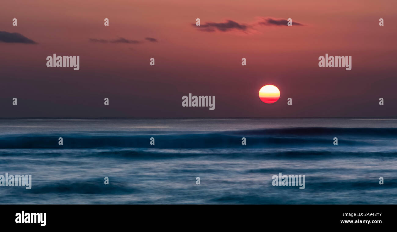 Il sole affonda sull'orizzonte dell'oceano con morbide onde ondulate; Kauai, Hawaii, Stati Uniti d'America Foto Stock