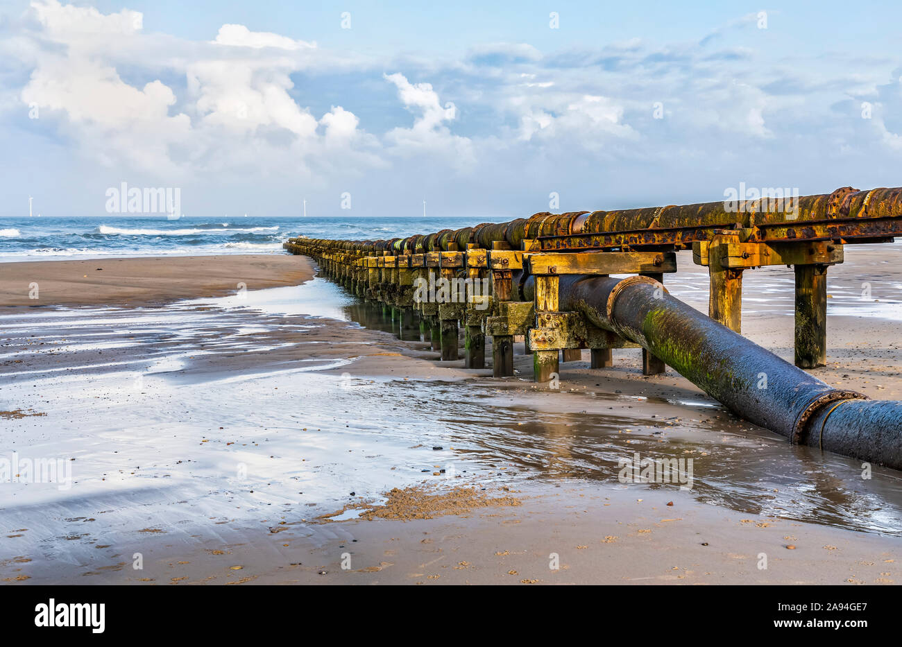 Tubi che trasportano rifiuti nel Mare del Nord a Cambogies Beach con turbine eoliche in lontananza; Northumberland, Inghilterra Foto Stock