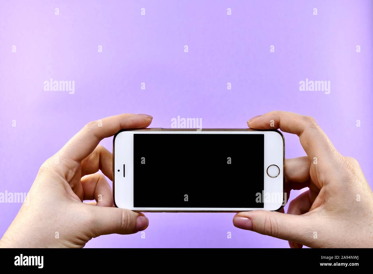 Uno smartphone con uno schermo nero in entrambe le mani su uno sfondo viola con posto per il testo. Foto Stock