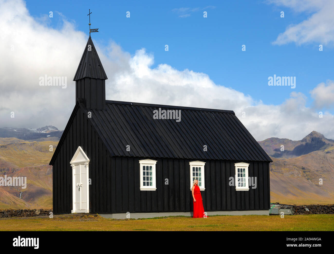 Signora in abito rosso Budir chiesa un nero struttura in legno dal 1847 seduto sulla penisola Snaefellsnese , Islanda Foto Stock