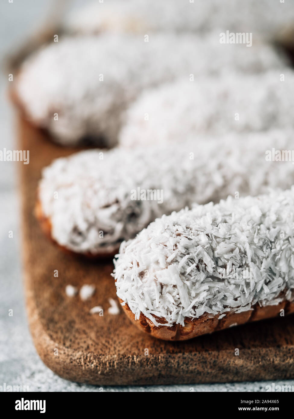 In casa eclairs con noce di cocco sul tagliere di legno. Vista ravvicinata della deliziosa profitroles sani con noce di cocco grattugiata. Copia spazio per il testo o il design. Verticale. Foto Stock