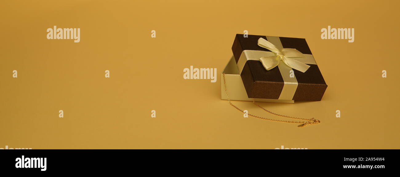 Piccolo decorativi scatola regalo, aperto a metà, con catena dorata e accanto al ravvicinato, isolato sul colore pastello giallo il colore dello sfondo. Foto Stock