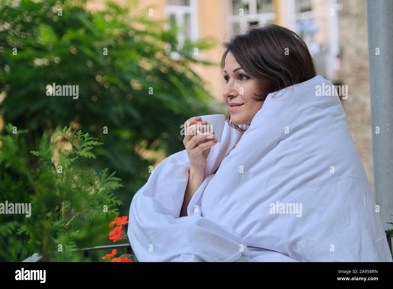 Sorridendo felice donna di mezza età con la tazza di caffè vestito in coperta Foto Stock