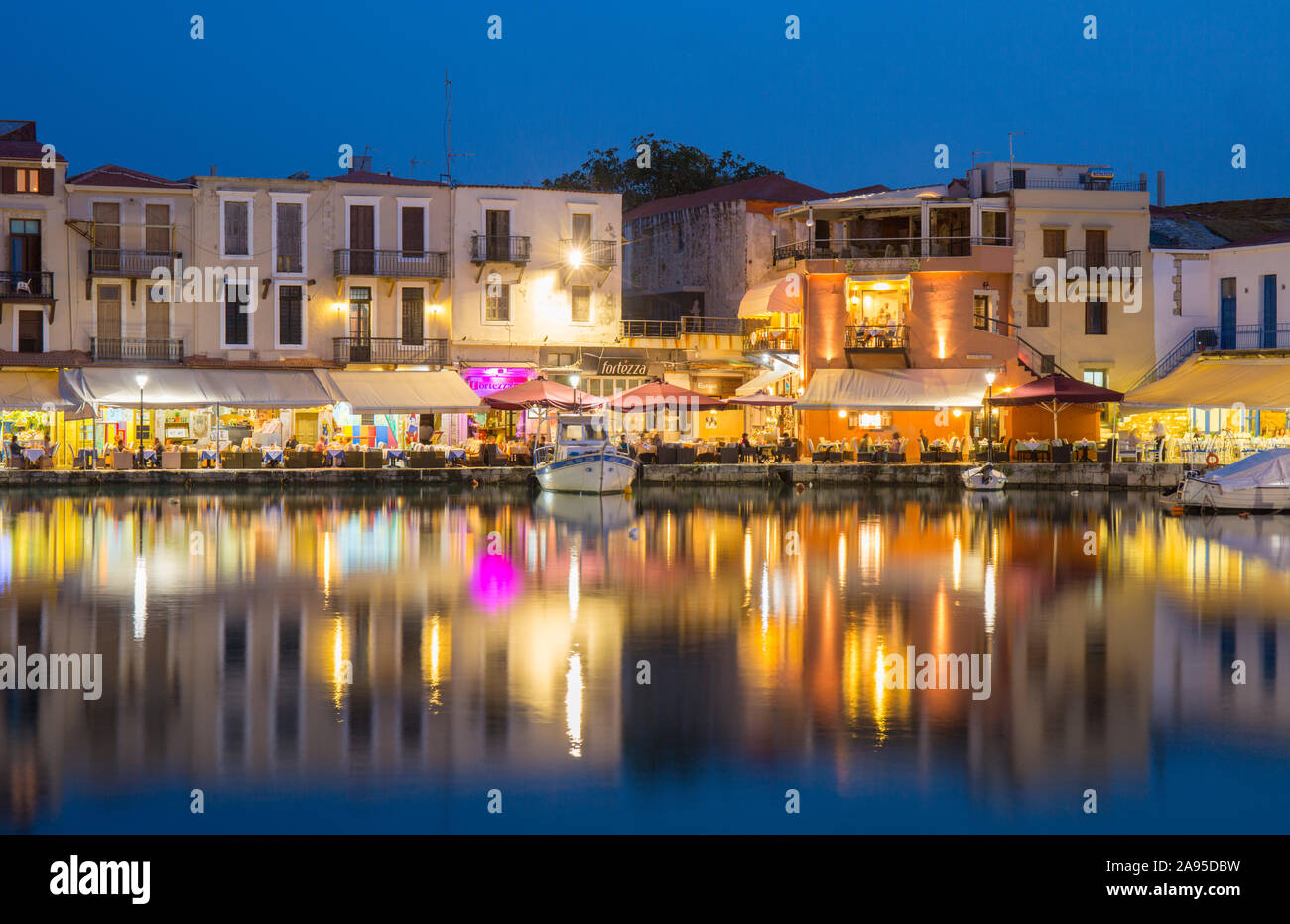 Rethymno, Creta, Grecia. Vista sul porto veneziano al crepuscolo, ristoranti luminosi che si riflettono nell'acqua. Foto Stock