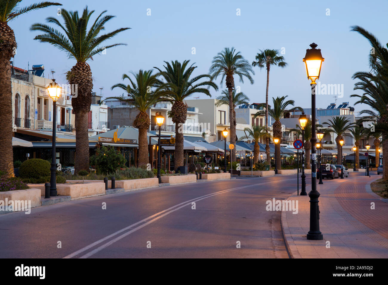 Rethymno, Creta, Grecia. Vista lungo il lungomare illuminato fiancheggiato da palme, Dawn. Foto Stock