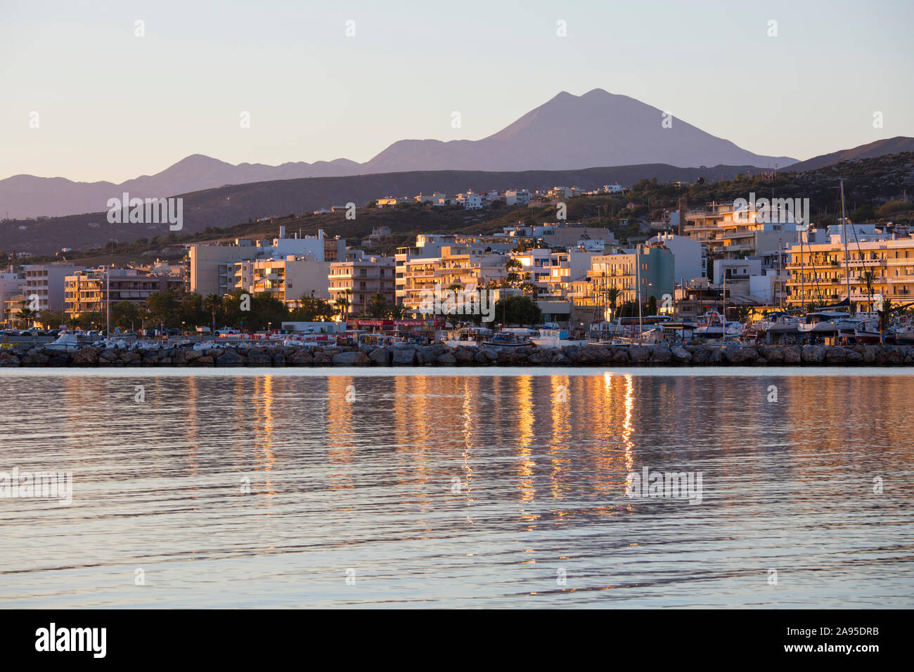Rethymno, Creta, Grecia. Gli edifici sul lungomare si riflettono nelle acque fisse, l'alba, il Monte Psiloritis visibile oltre. Foto Stock