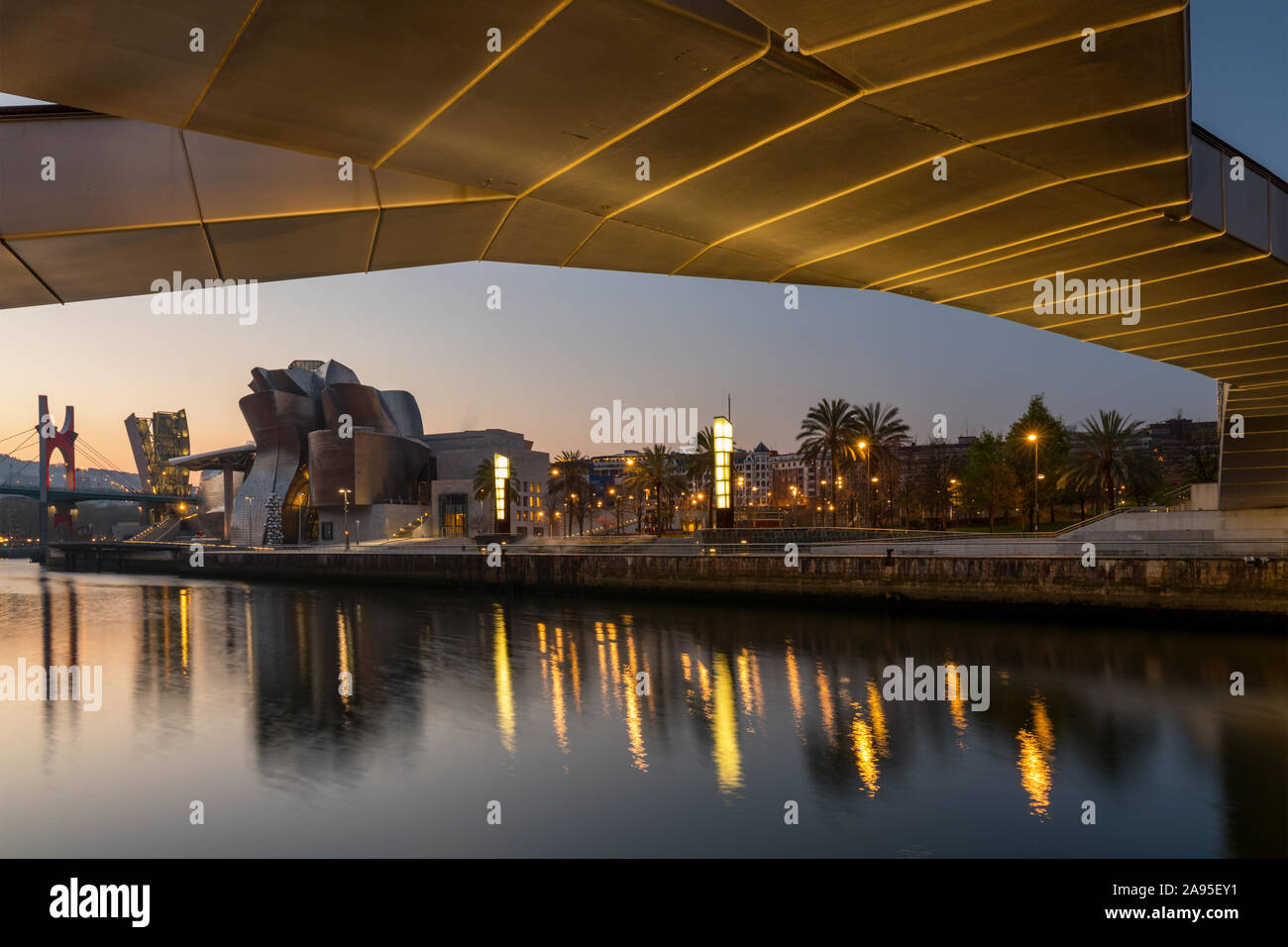 View all'alba attraverso il fiume Nervion verso l'illuminata Museo Guggenheim. Preso dal di sotto della Pasarela Pedro Arrupe bridge, Bilbao, Spagna Foto Stock