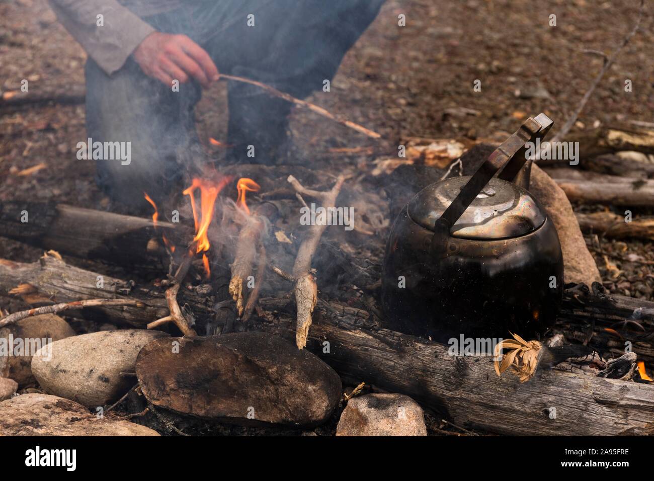 Bollitore per caffè sul fuoco, dietro di esso le gambe di una persona inginocchiata ai falò, Harjedalen, Svezia Foto Stock