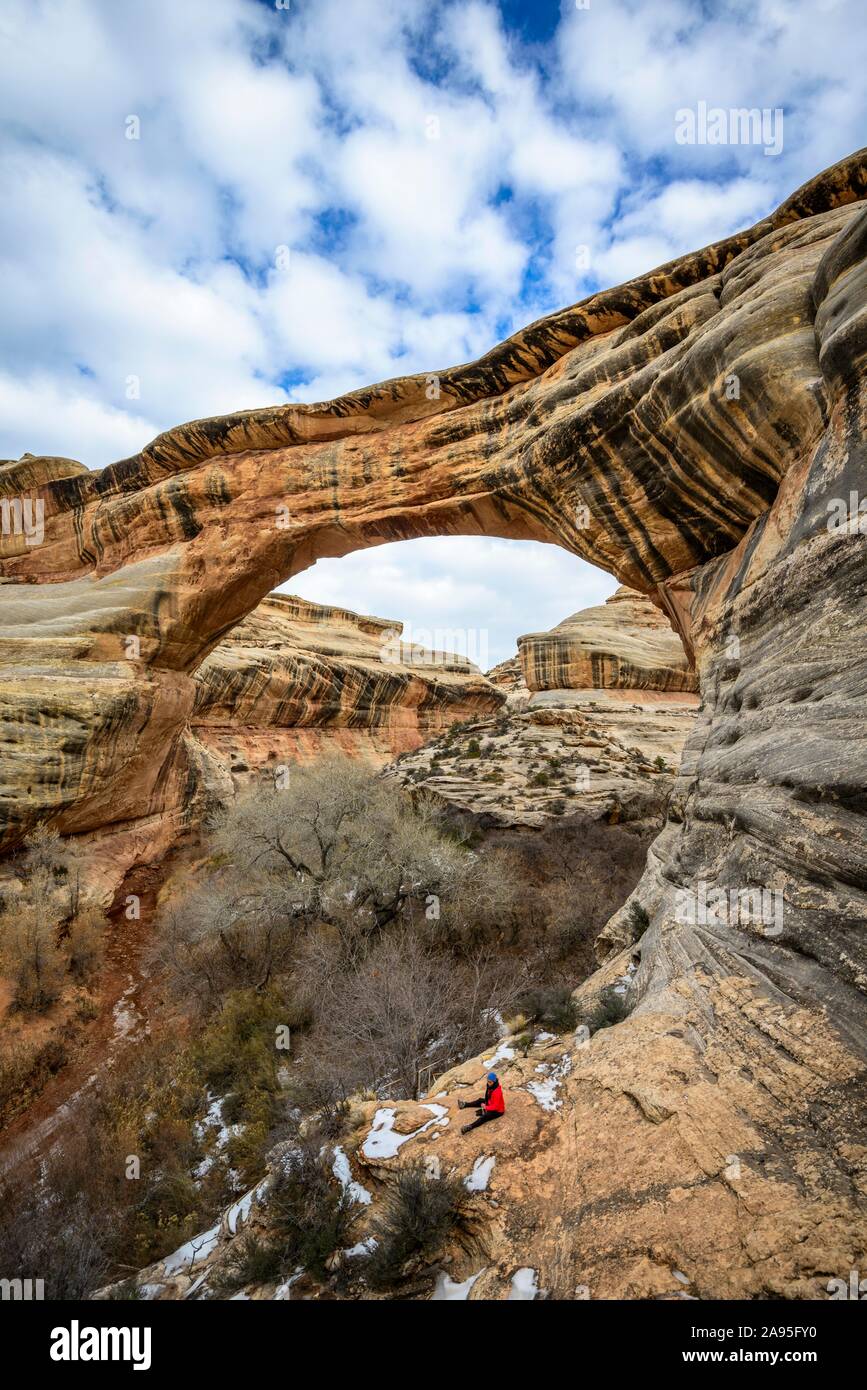 Tourist siede sotto roccia arch, Sipapu Bridge, ponti naturali monumento nazionale, Utah, Stati Uniti d'America Foto Stock