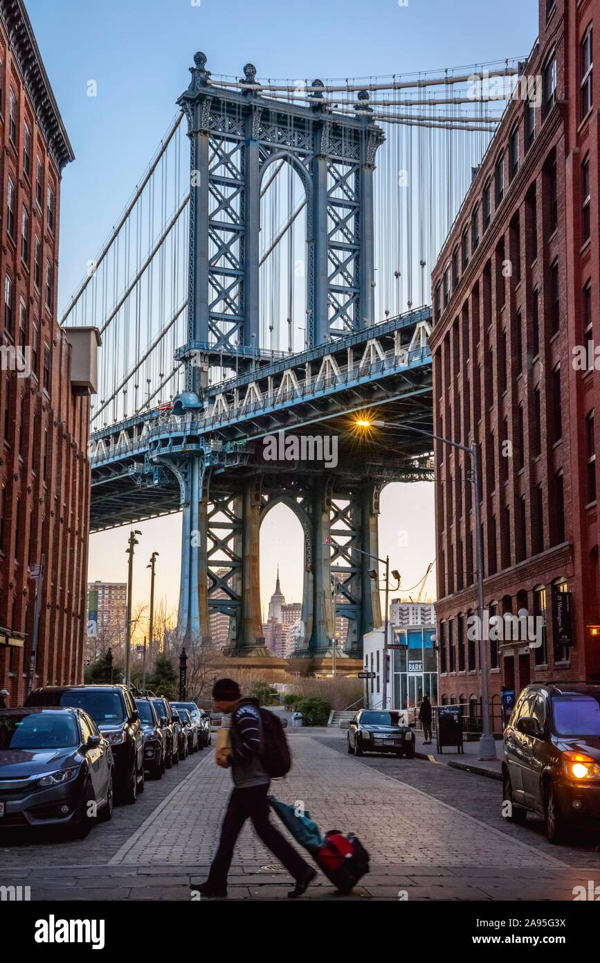 Turistico con valigia scorrevole attraversa la strada, vista dalla strada principale a Manhattan Bridge e Empire State Building, Atmosfera mattutina, Dumbo, Brooklyn Foto Stock