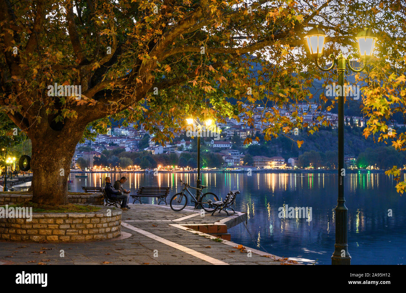 Luce della Sera Sul lungomare nord in Kastoria, guardando attraverso il lago Orestiada con la città sullo sfondo, Macedonia, Grecia settentrionale. Foto Stock