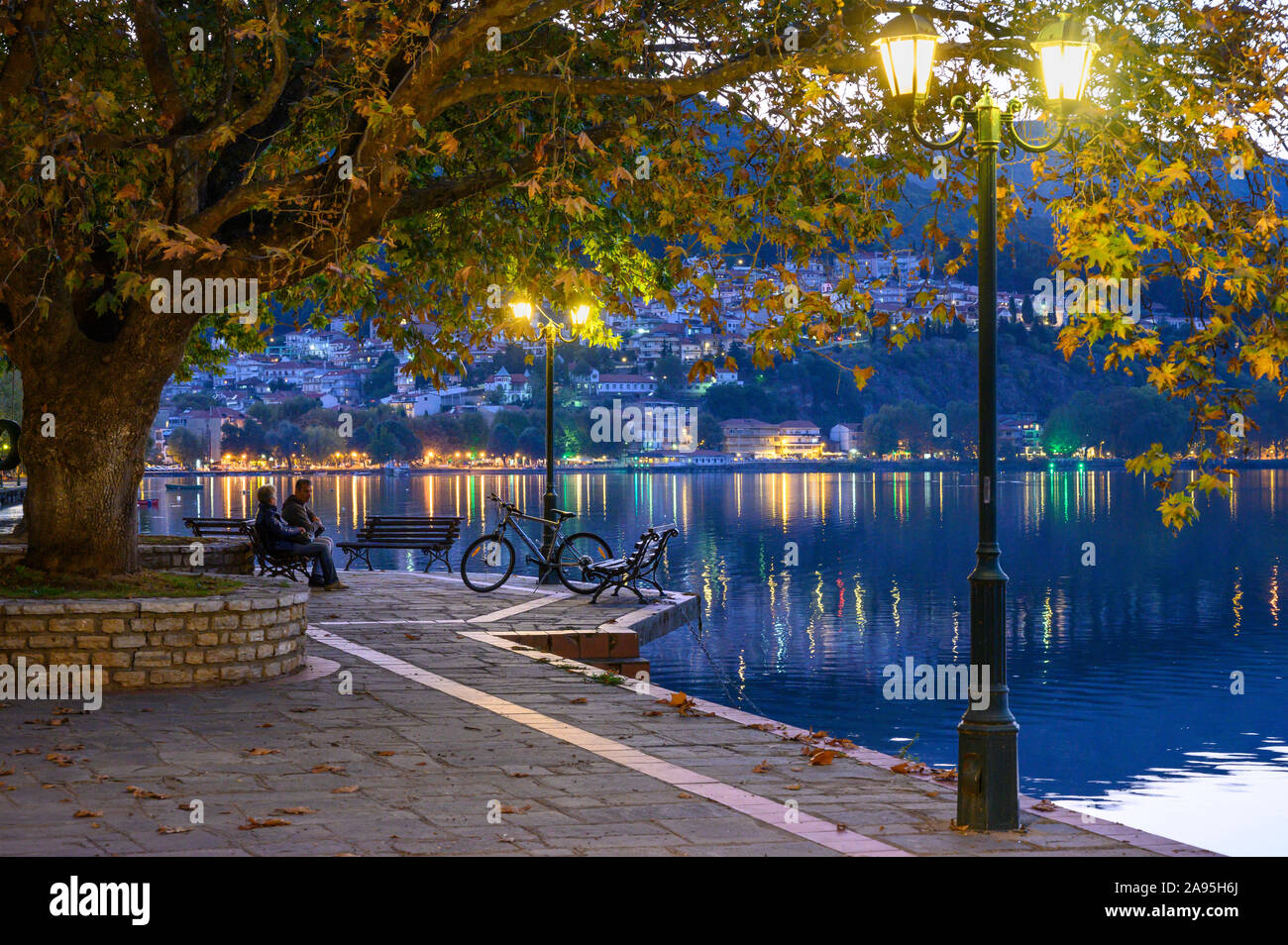 Luce della Sera Sul lungomare nord in Kastoria, guardando attraverso il lago Orestiada con la città sullo sfondo, Macedonia, Grecia settentrionale. Foto Stock