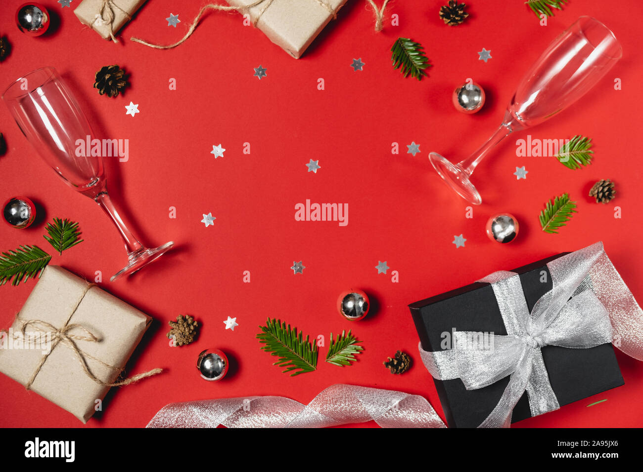 Vacanze di Natale composizione. Fatte a mano Scatole dono decorate con carta craft di Abete rami, due bicchieri di champagne, pini e coriandoli su rosso ba Foto Stock