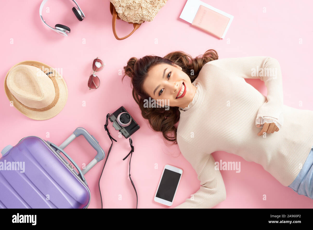 Bellezza ragazza asiatica giacente sul piano di colore rosa con tutti i bagagli di viaggio intorno a lei. Vista dall'alto. Foto Stock