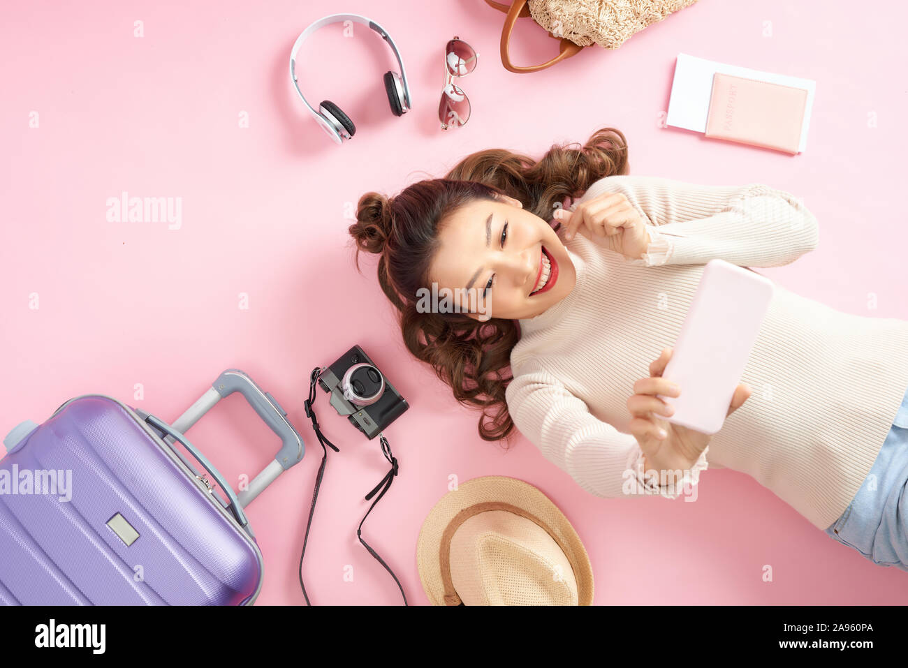 Bella giovane donna selfie sul pavimento di colore rosa con il suo bagaglio di viaggio. Vista superiore Foto Stock