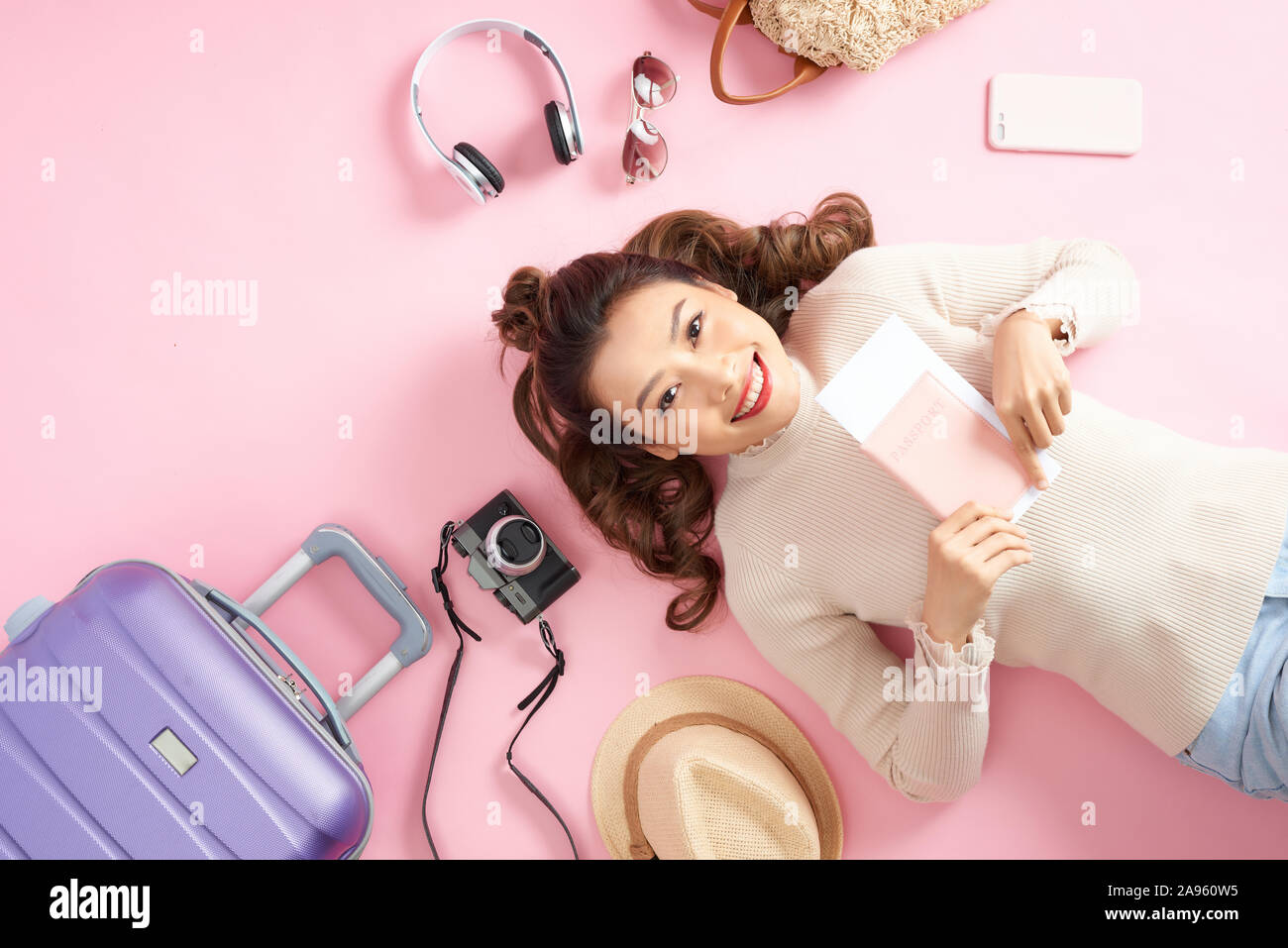 Giovane donna asiatica che mostra il suo passaporto mentre giaceva sul pavimento di colore rosa con bagaglio da viaggio surround. Vista superiore Foto Stock