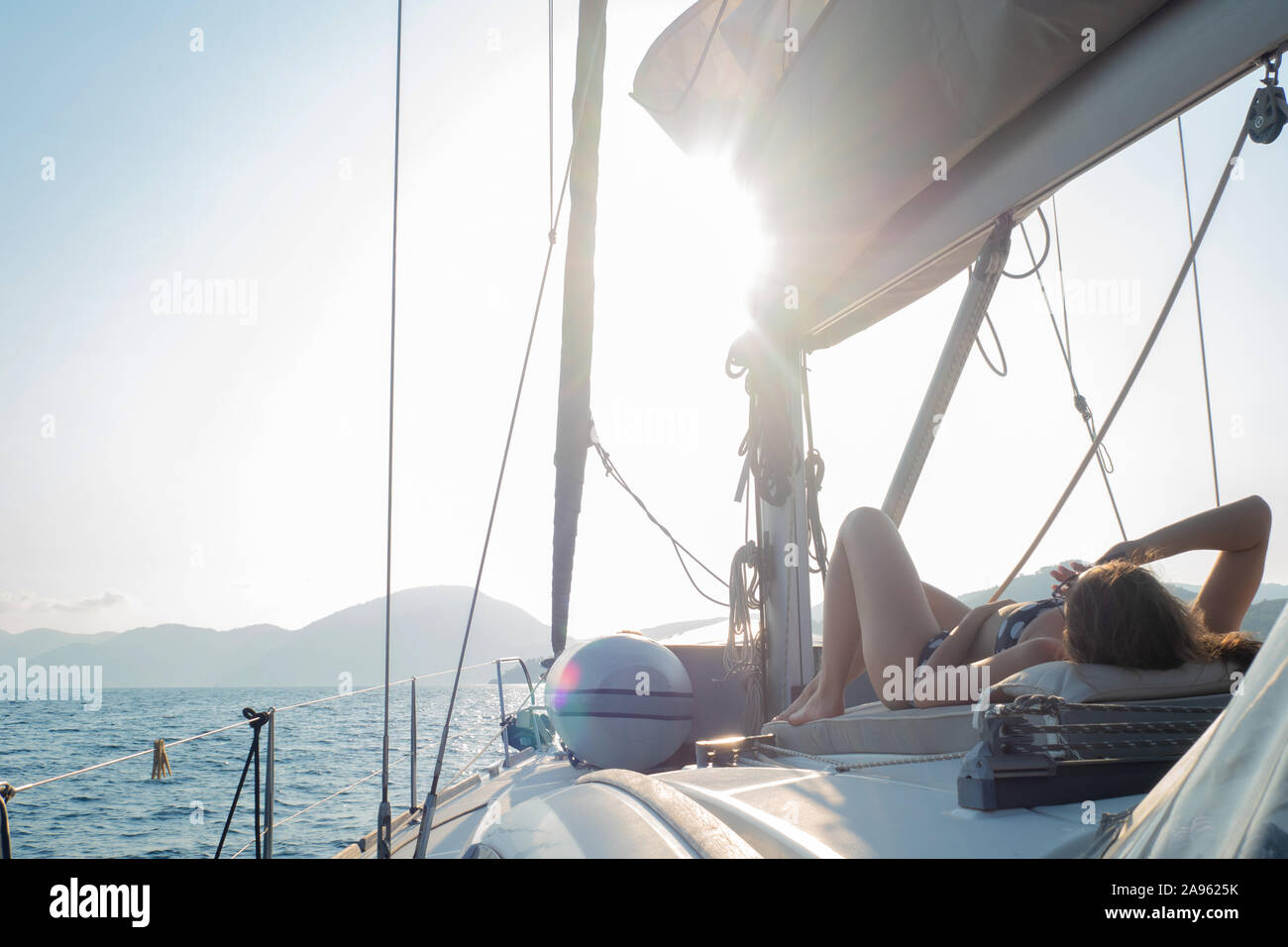 Gita in barca su uno yacht, una giovane donna a prendere il sole sul ponte di una barca a vela. Frammento del ponte. Foto Stock