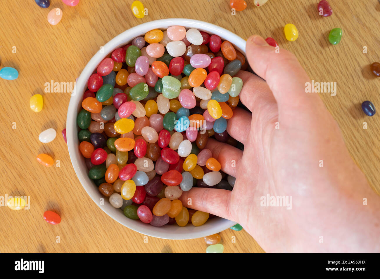 Un uomo adulto la mano scooping Jelly Beans in una ciotola piena di jellybeans. Concetto, la dipendenza da dolci, innamorate, candy, i piaceri della vita Foto Stock