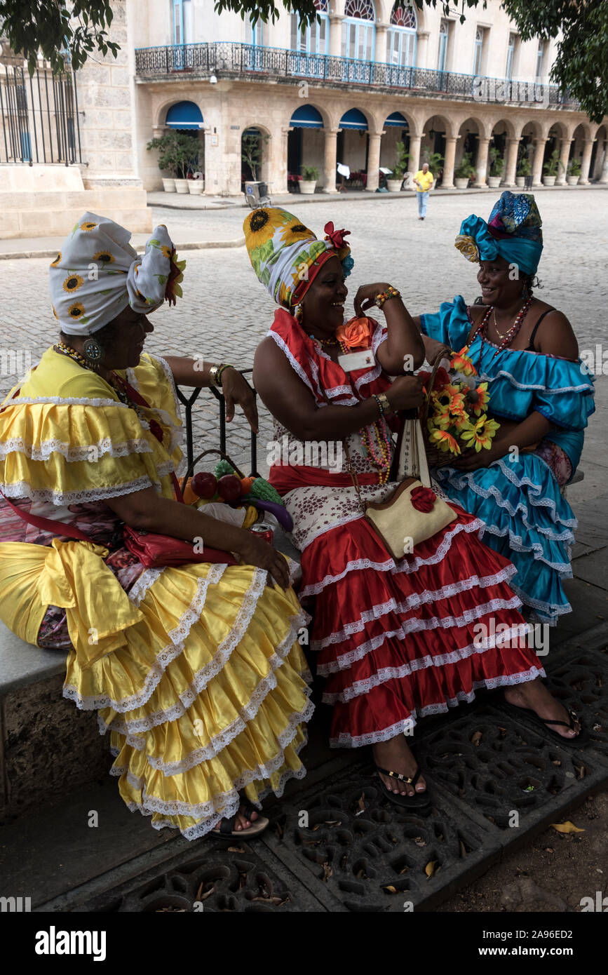 Un trio di donne cubane vestite con abiti coloniali dai colori vivaci, disposte a posare per fotografie turistiche per qualche moneta. Stanno prendendo una breve pausa Foto Stock