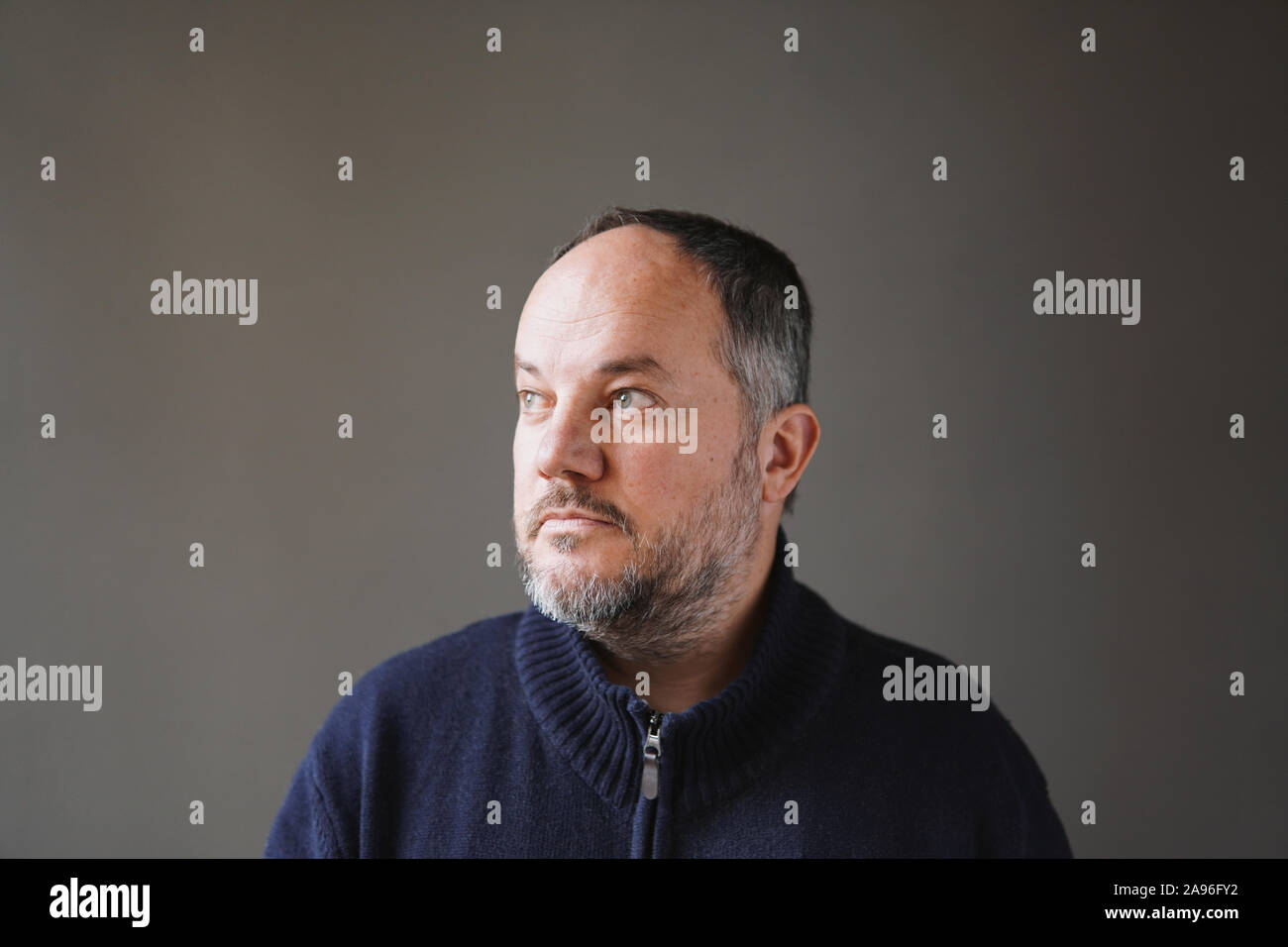 Uomo di 50 anni con l'ingrigimento dei capelli e barba che guarda lontano pensando - muro grigio Sfondo con spazio di copia Foto Stock