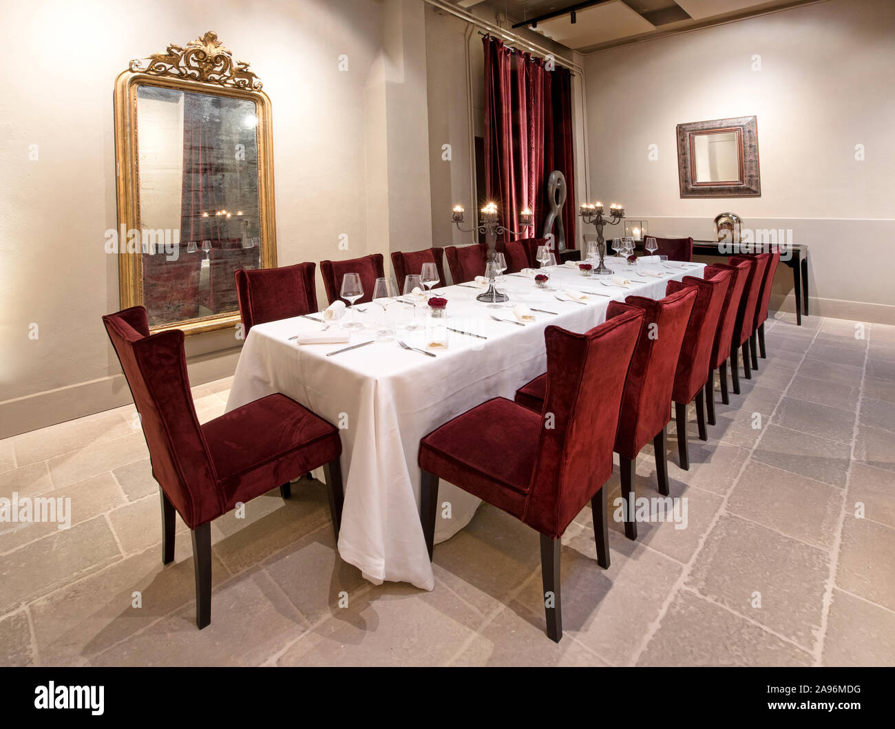 Formale lungo tavolo da pranzo in un ristorante elegante set con un panno bianco, posate e bicchieri con candele accese in candelabri Foto Stock