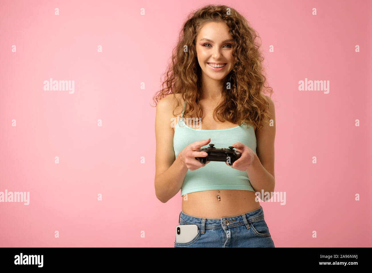 Pretty girl geek con capelli ricci azienda gamepad e riproduzione di videogioco isolato su sfondo rosa Foto Stock