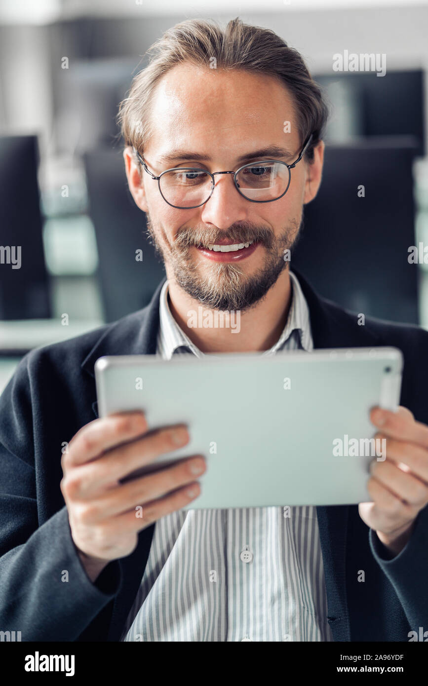 Giovane uomo bello in bicchieri di lettura di un tablet sul lavoro. Foto Stock