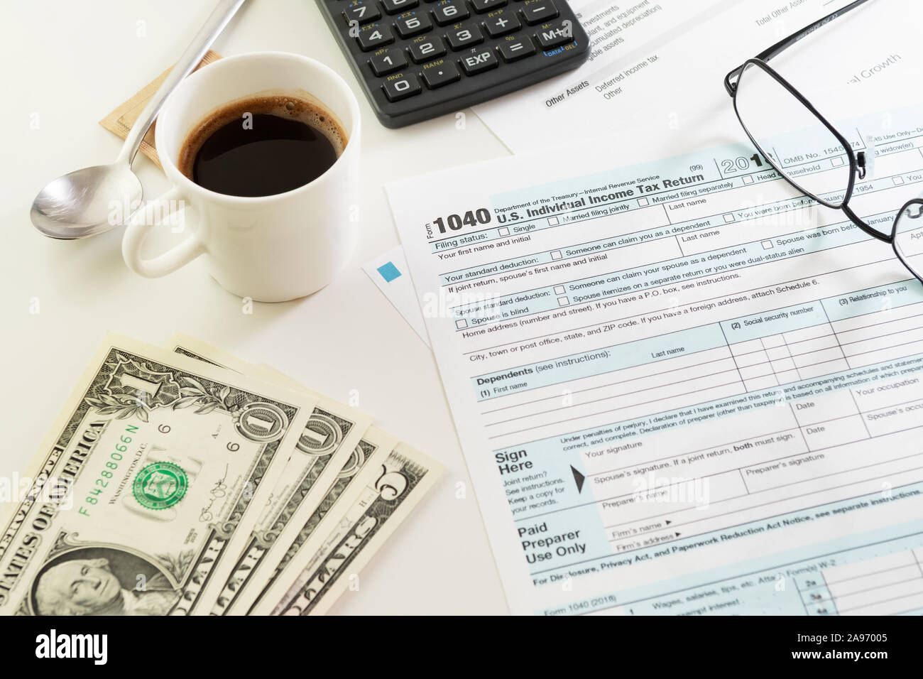 Stati Uniti Imposta sul reddito sotto forma di ritorno 1040 con il bianco tazza di caffè nero, cucchiaio, calcolatrice, occhiali e qualche dollaro banconote sul tavolo bianco. Imposta, IRS Foto Stock