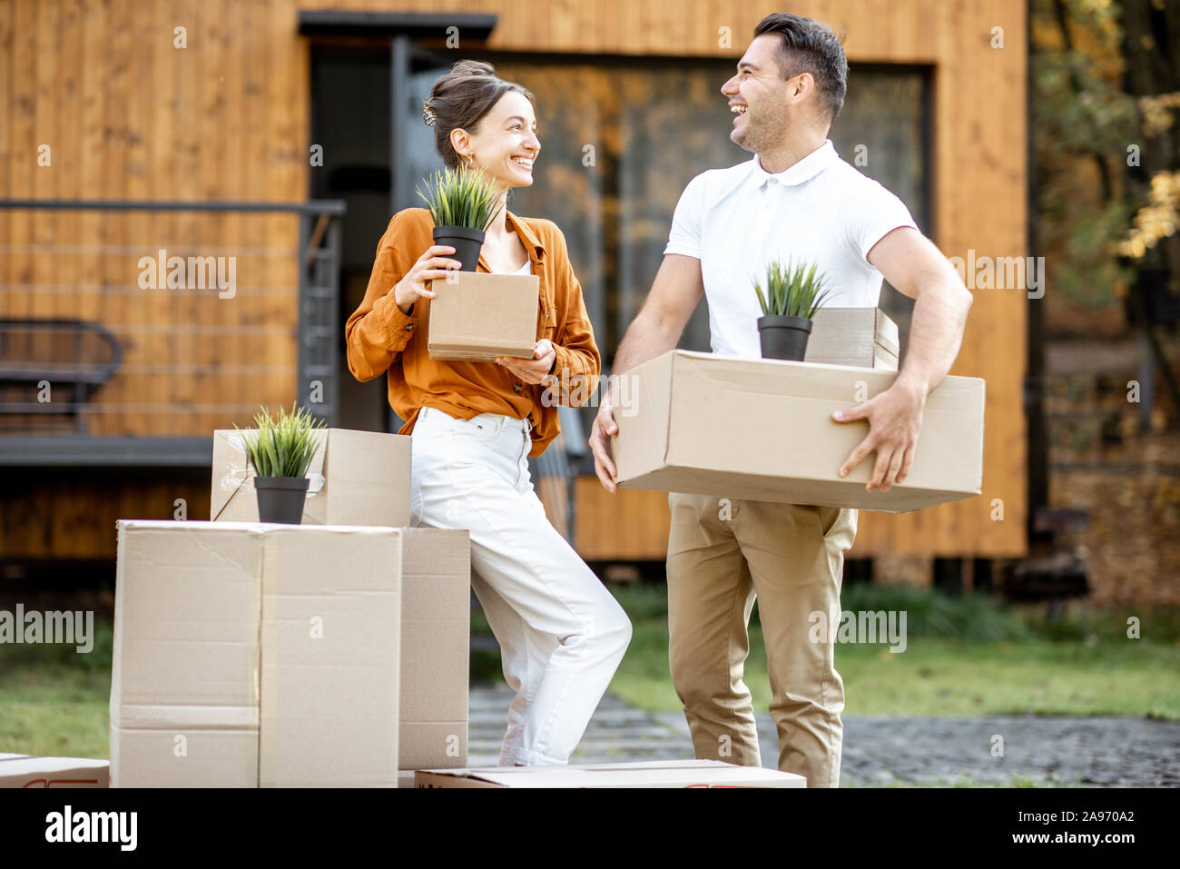 Ritratto di una felice coppia giovane in piedi con le scatole di cartone davanti alla loro nuova casa. Concetto di una delocalizzazione in una nuova casa Foto Stock