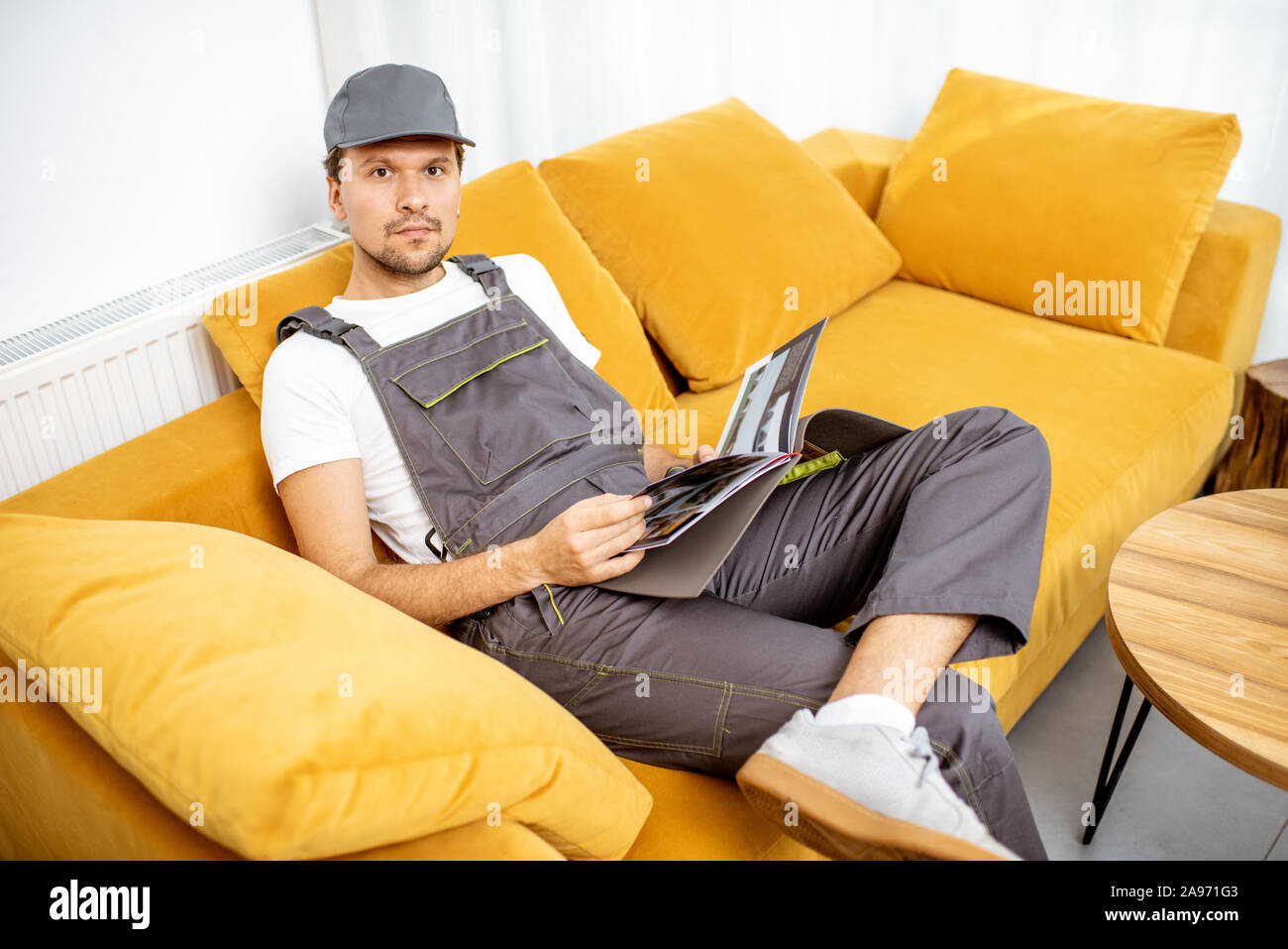 Tuttofare in workwear seduto sul divano giallo durante il riposo dopo il lavoro Foto Stock
