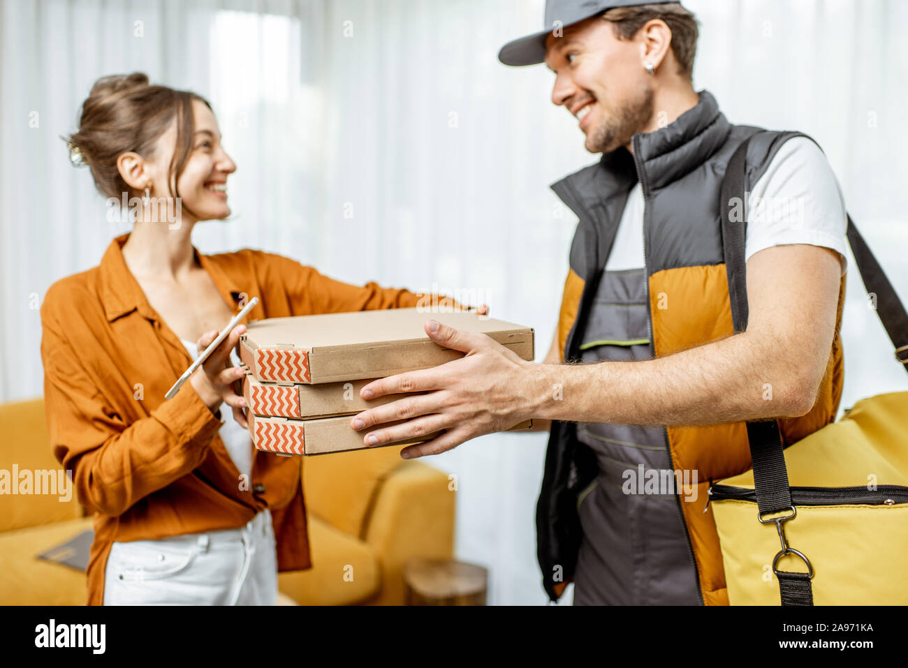 Bello corriere in uniforme garantendo la pizza con borsa termica per un client home, donna felice ricevere il suo ordine Foto Stock