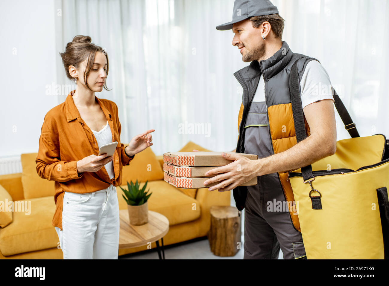 Bello corriere in uniforme garantendo la pizza con borsa termica per un client home, donna felice ricevere il suo ordine Foto Stock