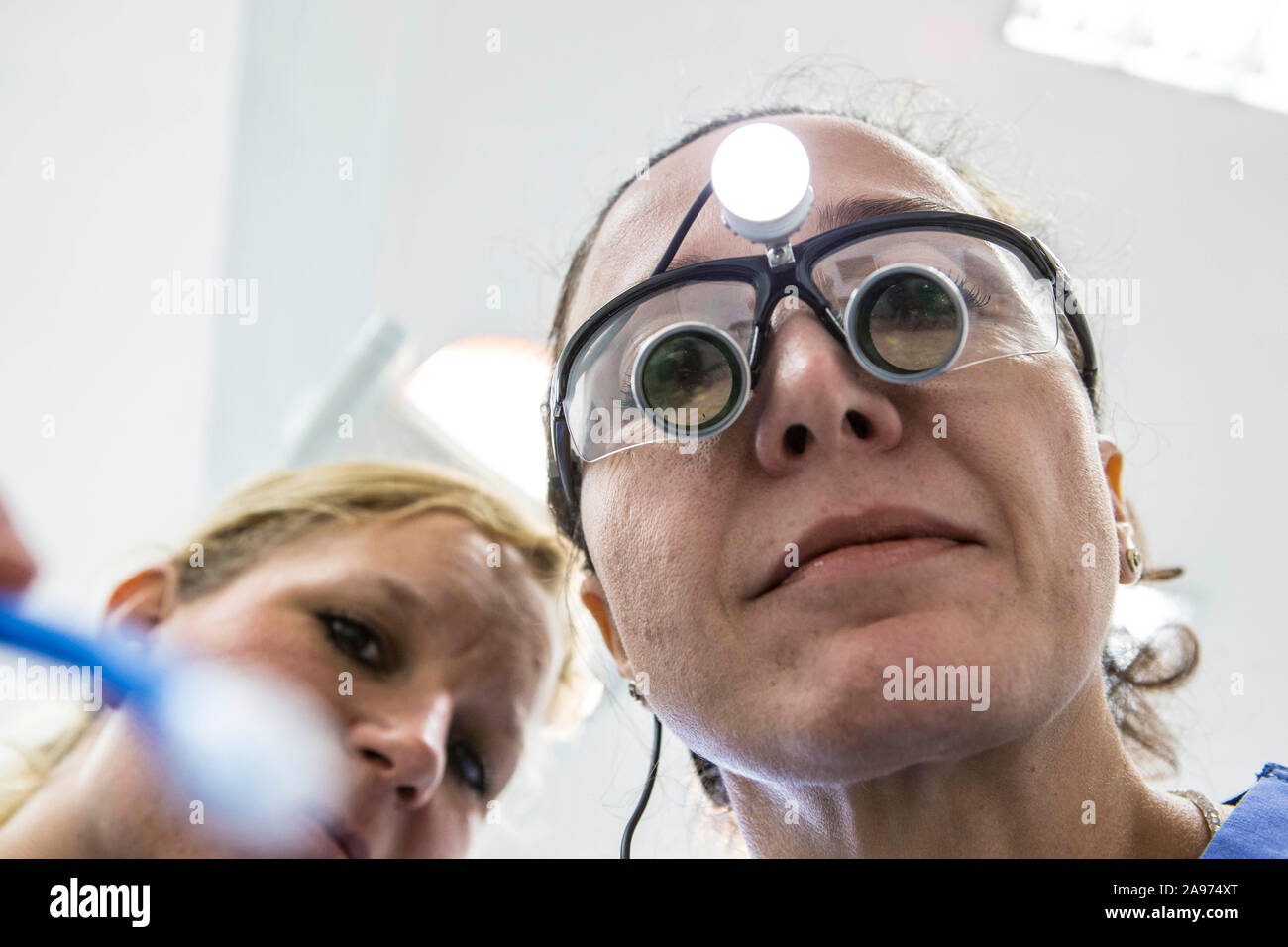 Eine Zahnärztin trägt bei der Behandlung ihrer Patienten eine Lupenbrile. Diese beleuchtete Spezialbrille hat eine Schutzwirkung gegen Splitter beim B Foto Stock