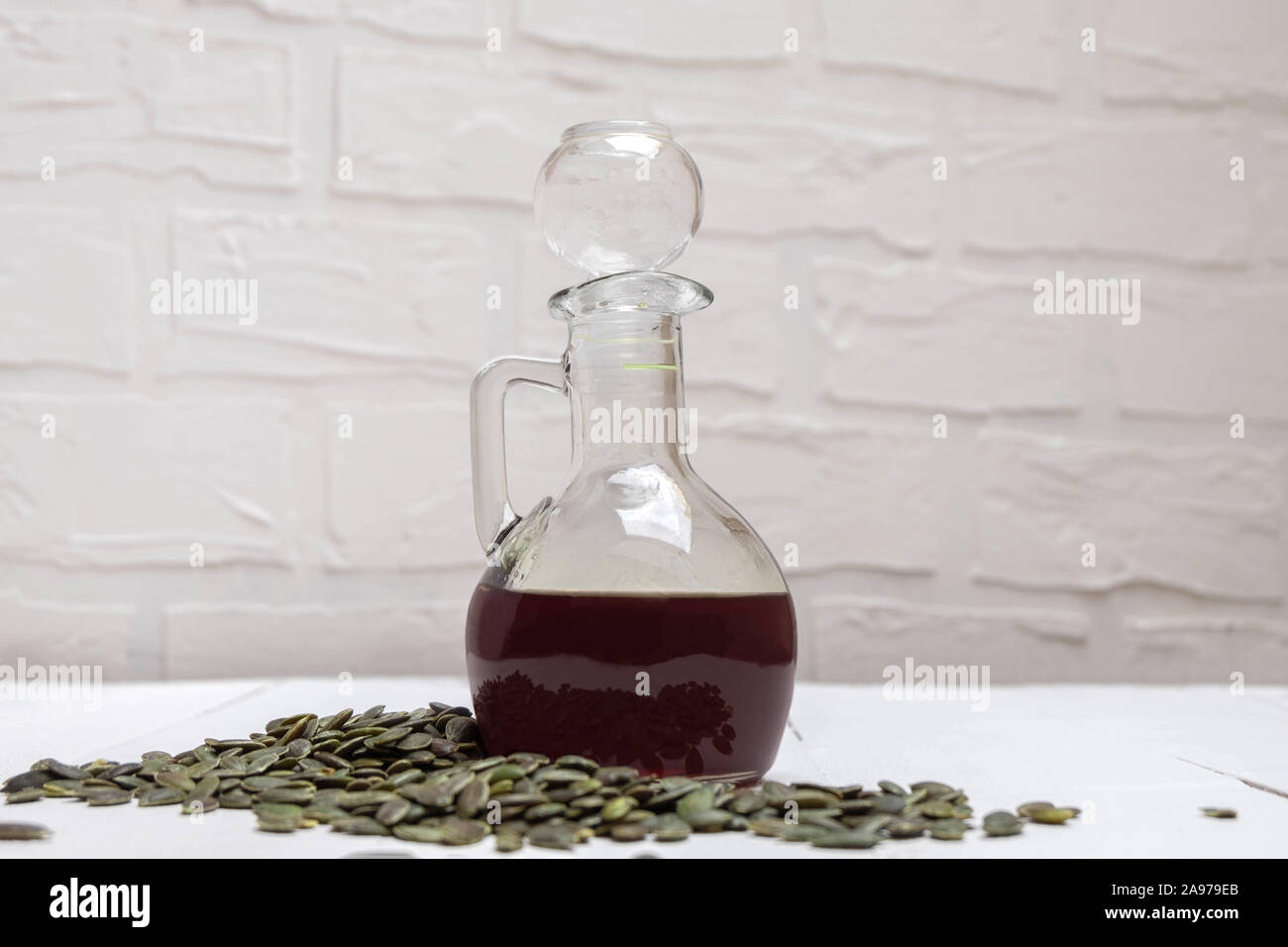 Bottiglia di vetro dell'olio di semi di zucca con semi di zucca su bianco tavolo in legno Foto Stock