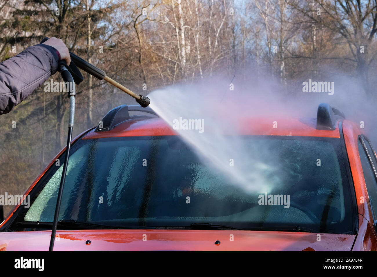La pulizia con acqua a self-service car wash. L'uomo lava parabrezza nella sua vettura arancione. Acqua saponata scorre verso il basso. Foto Stock