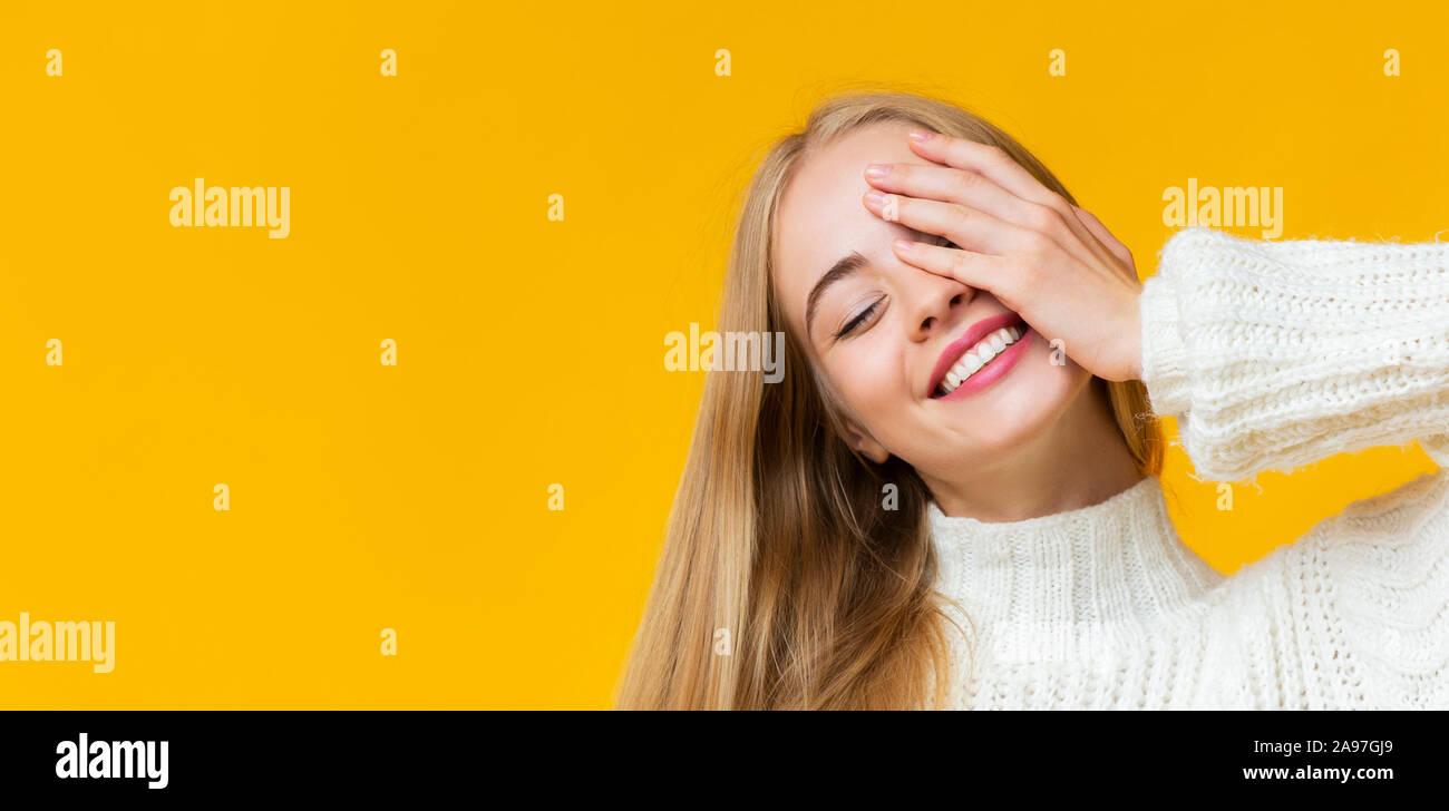 Ritratto di bella ragazza con gli occhi chiusi che posano su sfondo giallo per coprire un occhio con palm, panorama con spazio di copia Foto Stock