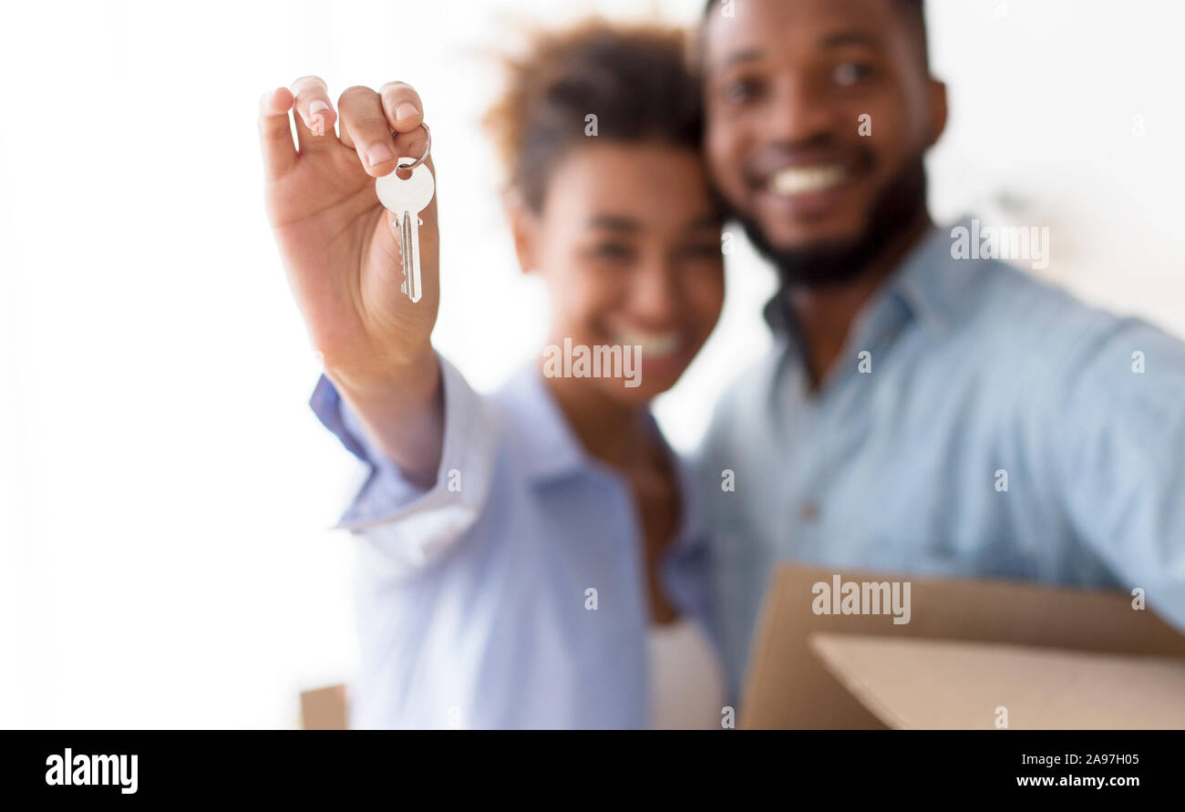 Nuova casa. Felice coppia Afro che mostra i tasti abbracciando dopo lo spostamento in casa propria Standing Indoor. Messa a fuoco selettiva, Profondità minima Foto Stock