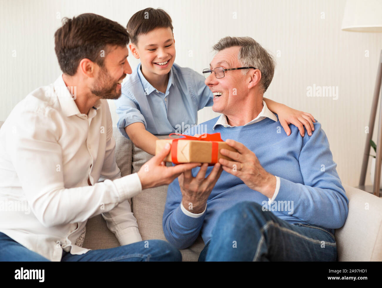 Nonno il compleanno. Coppia, figlio e nipote congratulandosi con il nonno dandogli dono seduti sul divano di casa. Messa a fuoco selettiva Foto Stock